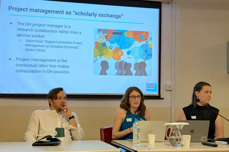 Three panelists sit in front of a PowerPoint presentation.