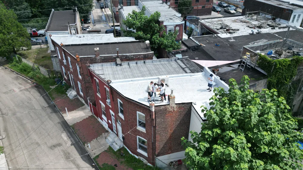 Aerial view of 5 people on the roof of a brick row home, holding an antenna.