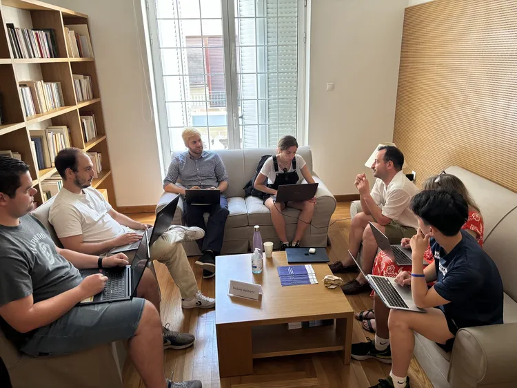 A group of people with laptops gather around a coffee table