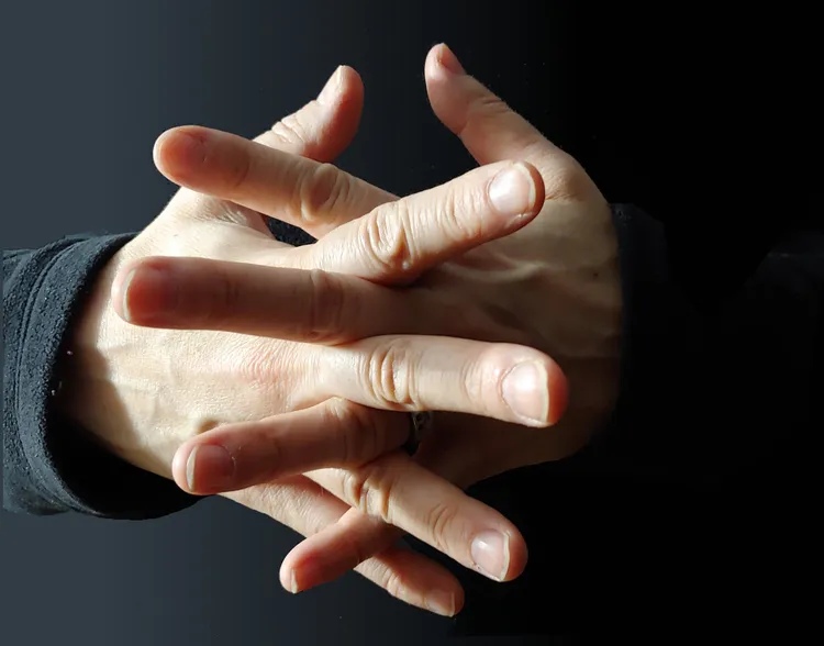 close up of a person's hands with fingers interleaved and crossing each other